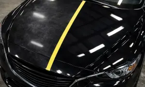 Czarne auto z żółtym pasem dzielącym matową, porysowaną maskę od błyszczącej, lustrzanej.