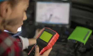 Mechanik z urządzeniem diagnostycznym i laptopem w tle.