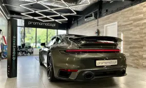 Ciemnozielone Porsche 911 w garażu z nowoczesnym oświetleniem i stojącym obok produktem Rivashield.