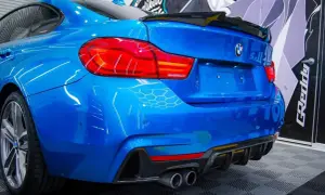 Niebieskie BMW z czarnym spoilerem na klapie bagażnika i dyfuzorem z włókna węglowego.