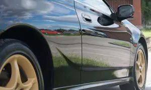 Błyszczący, czarny samochód z odbiciami nieba i innych aut.