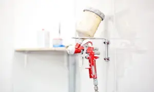 Czerwony pistolet lakierniczy z pojemnikiem na farbę, zawieszony na ścianie.