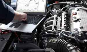 Ręka na klawiaturze laptopa podłączonego do silnika samochodu, na ekranie wykresy.
