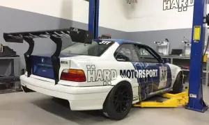 BMW E36 coupe z dużym spojlerem na podnośniku w warsztacie.