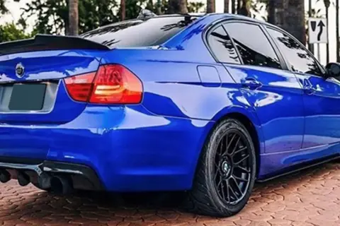Niebieskie BMW E90 z czarnym spoilerem na klapie bagażnika i dyfuzorem.