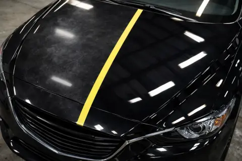Czarne auto z żółtym pasem dzielącym matową, porysowaną maskę od błyszczącej, lustrzanej.
