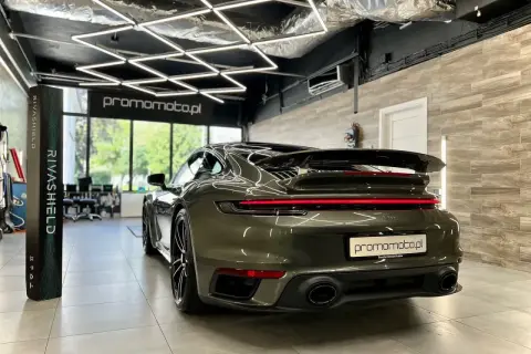 Ciemnozielone Porsche 911 w garażu z nowoczesnym oświetleniem i stojącym obok produktem Rivashield.