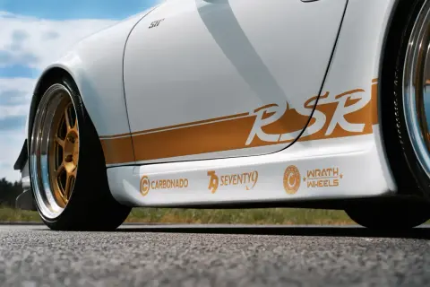 Biały samochód z pomarańczowymi naklejkami "RSR", "CARBONADO", "SEVENTY9" i "WRATH WHEELS".