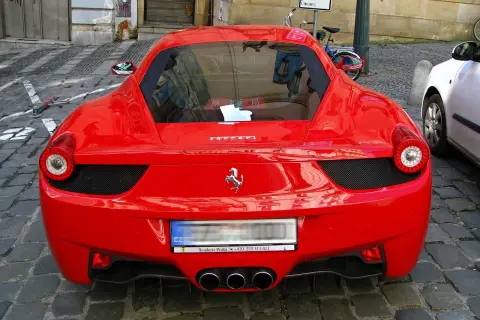 Czerwone Ferrari z widocznym logo konia, na brukowanej ulicy.