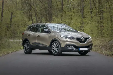 Złoty SUV stoi na drodze w lesie z zielonymi drzewami w tle.