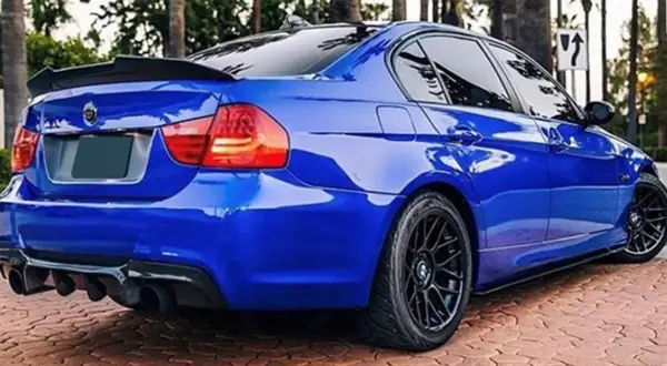 Niebieskie BMW E90 z czarnym spoilerem na klapie bagażnika i dyfuzorem.