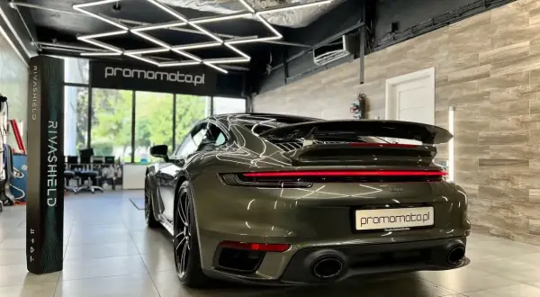 Ciemnozielone Porsche 911 w garażu z nowoczesnym oświetleniem i stojącym obok produktem Rivashield.