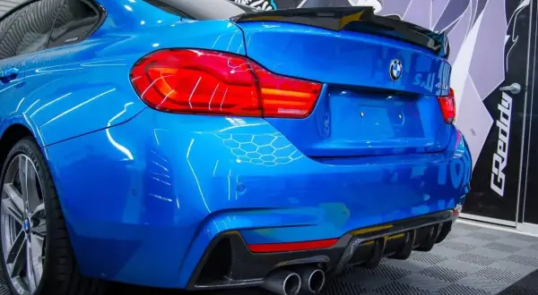 Niebieskie BMW z czarnym spoilerem na klapie bagażnika i dyfuzorem z włókna węglowego.