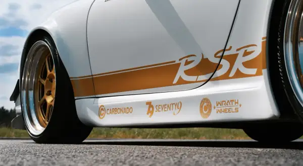 Biały samochód z pomarańczowymi naklejkami "RSR", "CARBONADO", "SEVENTY9" i "WRATH WHEELS".