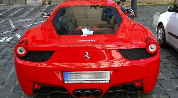 Czerwone Ferrari z widocznym logo konia, na brukowanej ulicy.