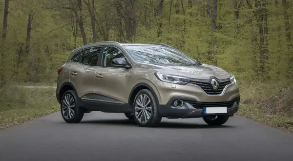 Złoty SUV stoi na drodze w lesie z zielonymi drzewami w tle.