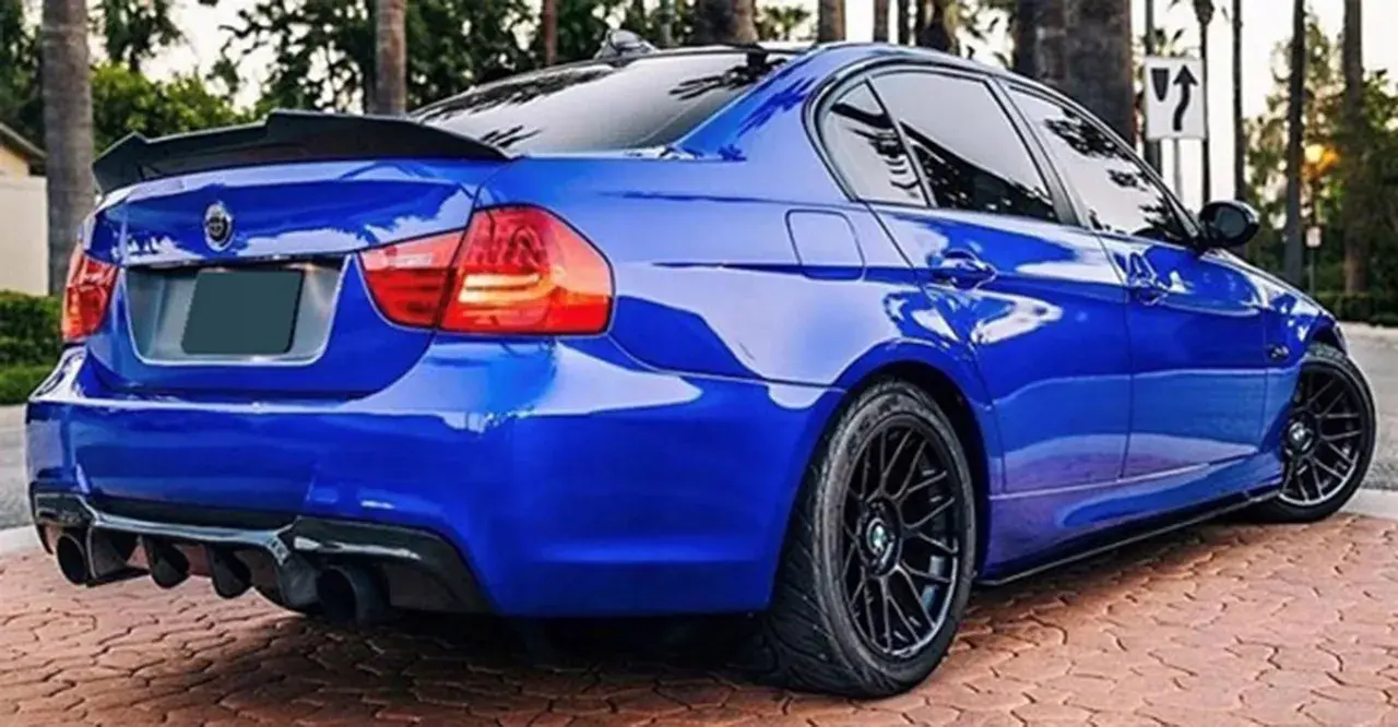 Niebieskie BMW E90 z czarnym spoilerem na klapie bagażnika i dyfuzorem.