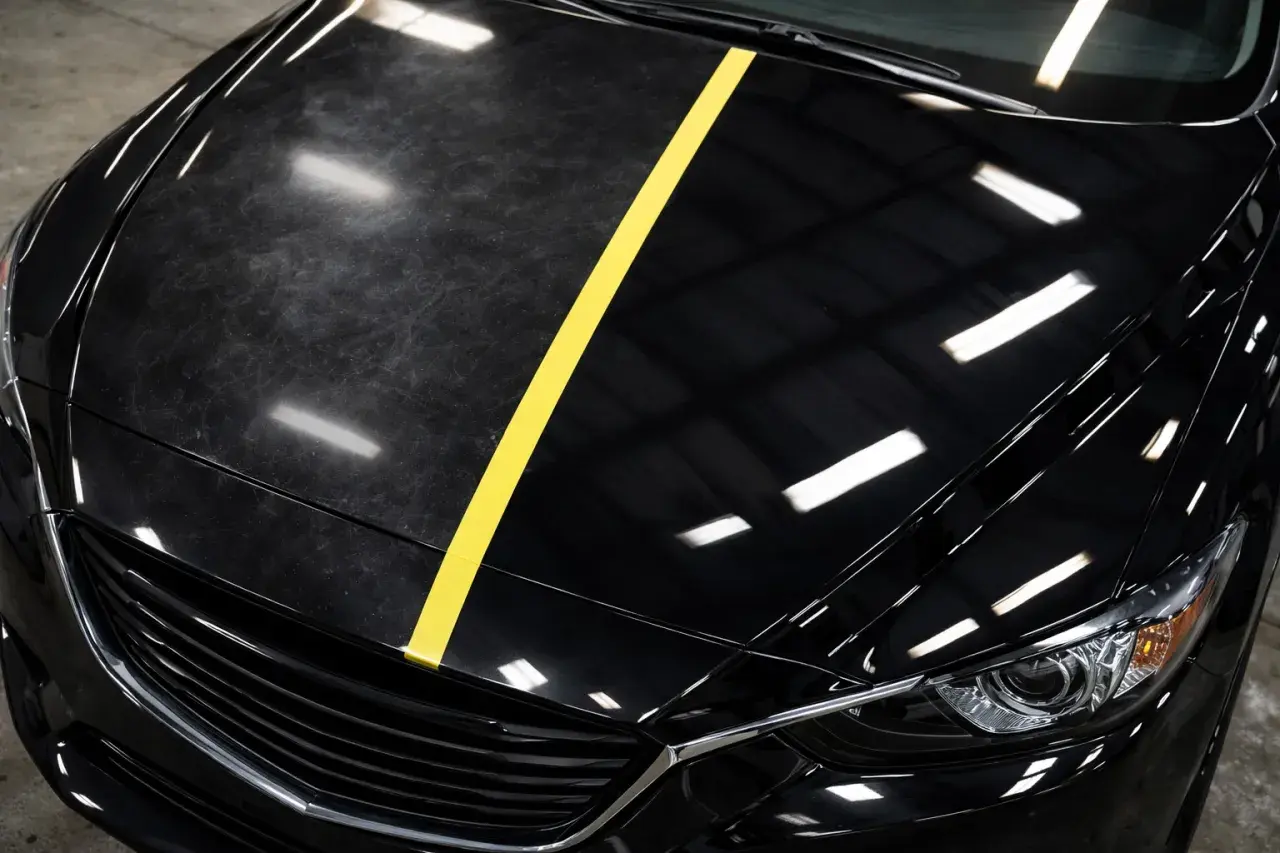 Czarne auto z żółtym pasem dzielącym matową, porysowaną maskę od błyszczącej, lustrzanej.