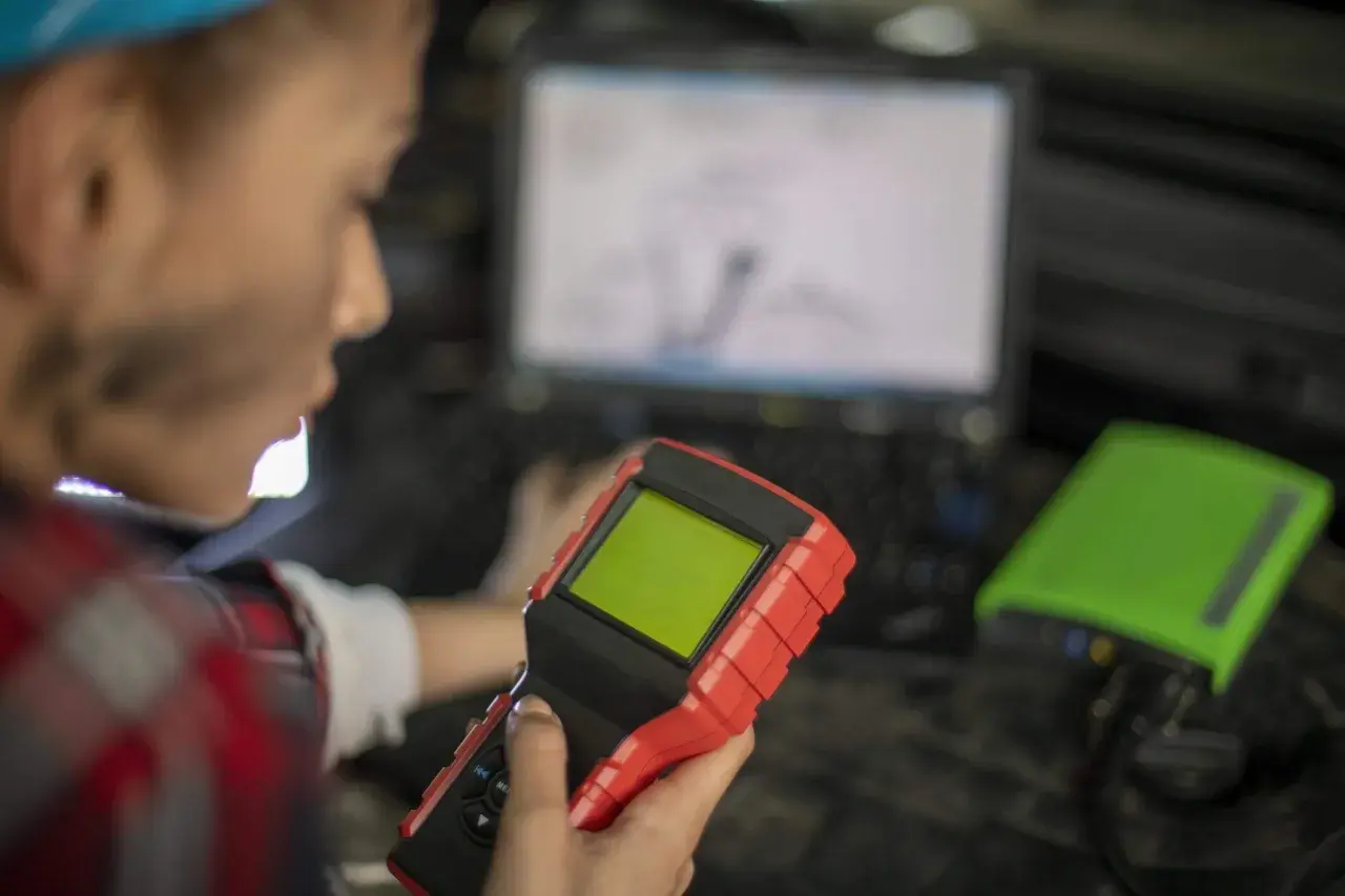 Mechanik z urządzeniem diagnostycznym i laptopem w tle.