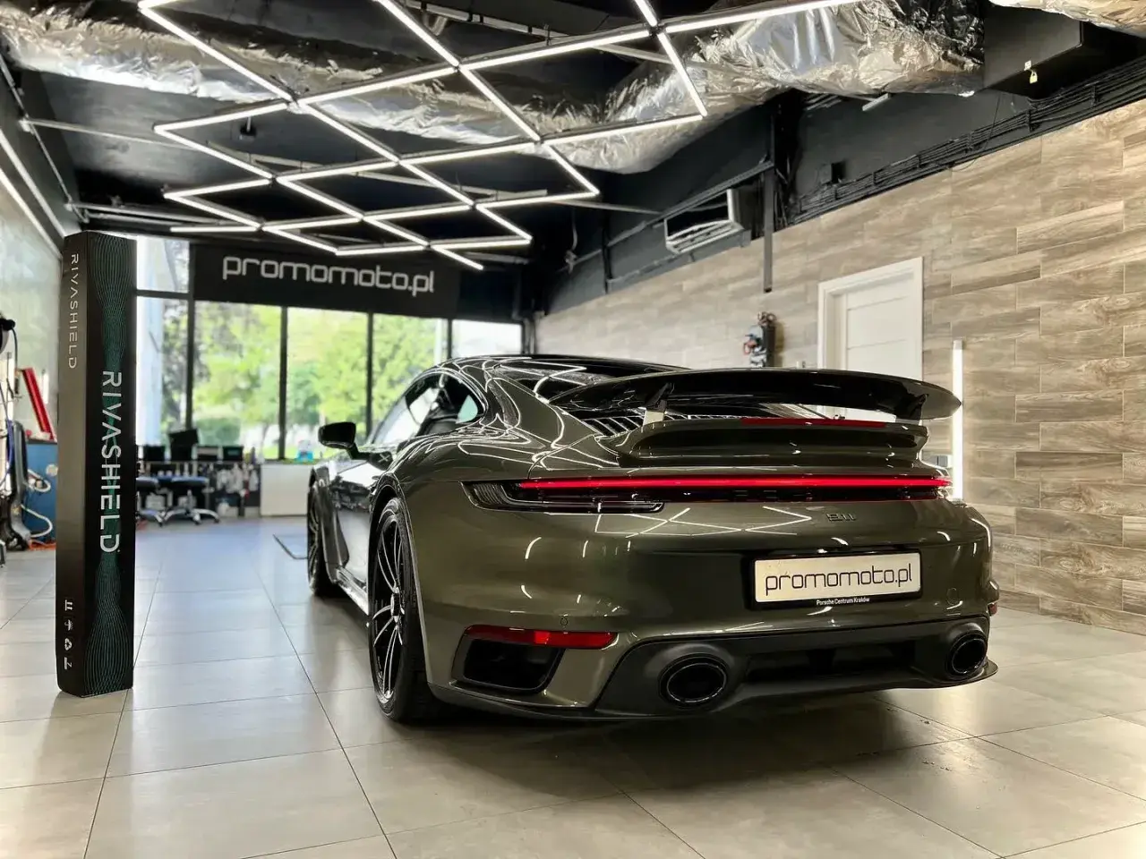Ciemnozielone Porsche 911 w garażu z nowoczesnym oświetleniem i stojącym obok produktem Rivashield.