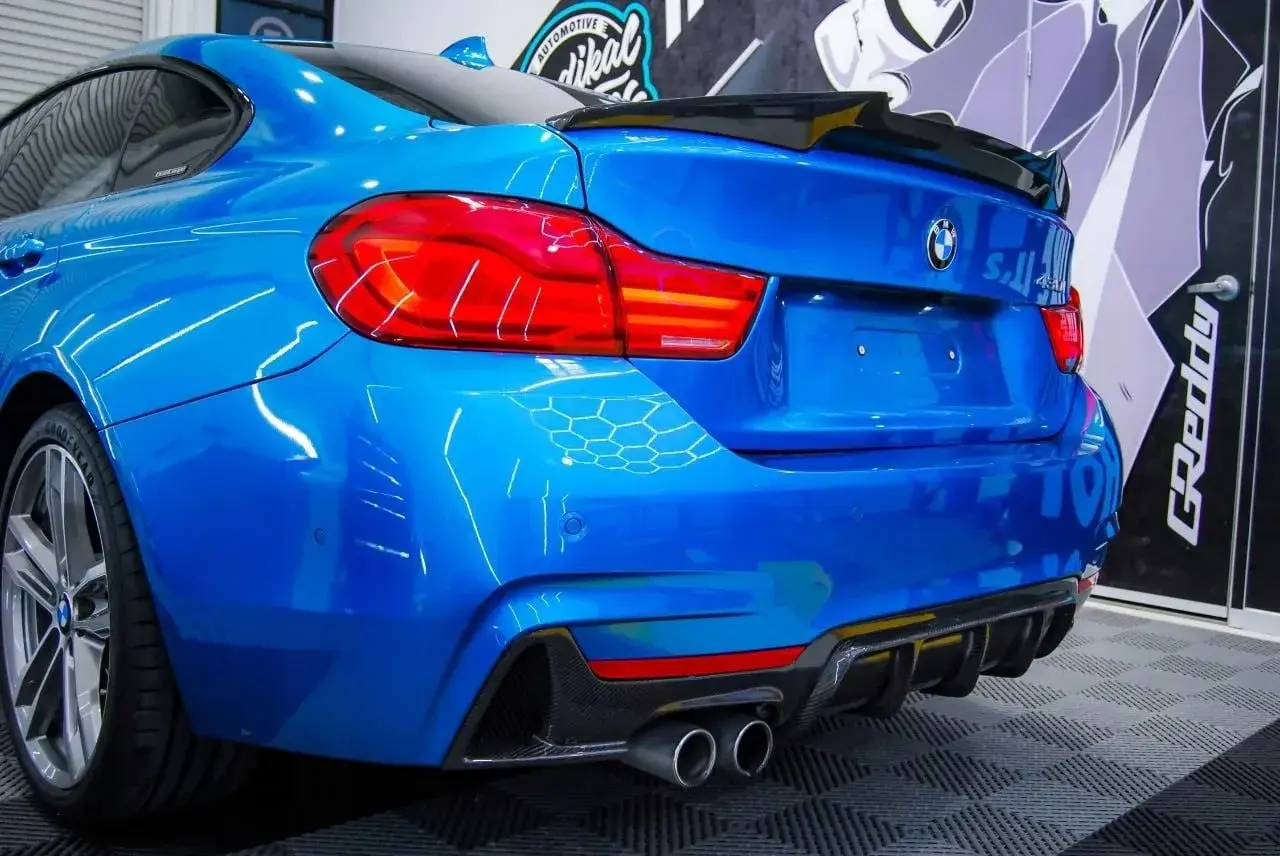 Niebieskie BMW z czarnym spoilerem na klapie bagażnika i dyfuzorem z włókna węglowego.