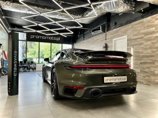 Ciemnozielone Porsche 911 w garażu z nowoczesnym oświetleniem i stojącym obok produktem Rivashield.