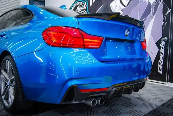 Niebieskie BMW z czarnym spoilerem na klapie bagażnika i dyfuzorem z włókna węglowego.