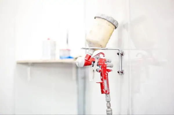 Czerwony pistolet lakierniczy z pojemnikiem na farbę, zawieszony na ścianie.