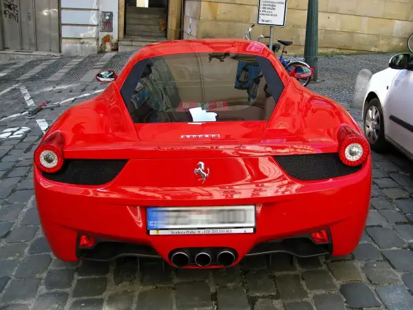 Czerwone Ferrari z widocznym logo konia, na brukowanej ulicy.