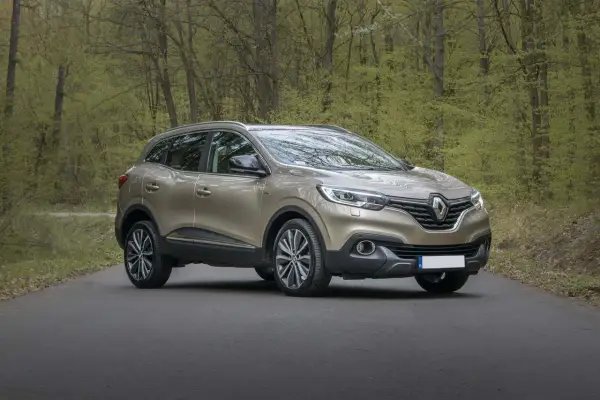 Złoty SUV stoi na drodze w lesie z zielonymi drzewami w tle.